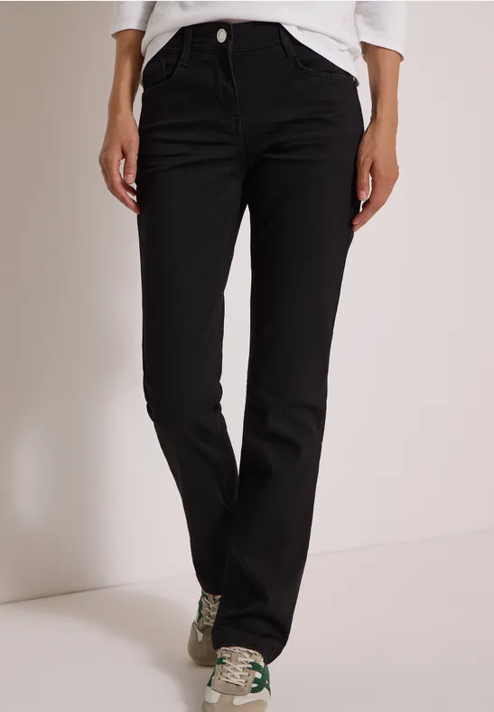 Pantalon noir droit porté par une personne debout en baskets sur fond clair