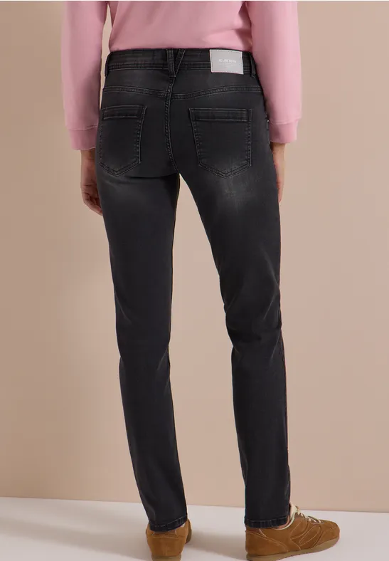 Rückansicht einer Person in dunklen Jeans, rosa Pullover und braunen Schuhen.