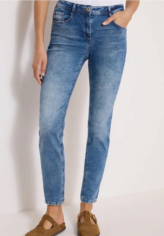 Blaue, eng anliegende Jeans bis zum Knöchel, kombiniert mit braunen Wildleder-Pantoletten.
