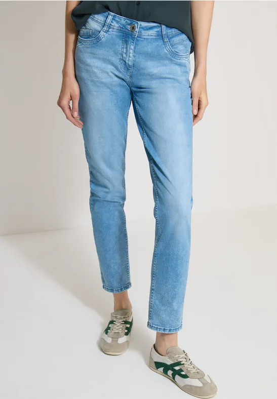 Une personne porte un jean bleu clair ajusté, un top noir et des baskets blanc-vert.
