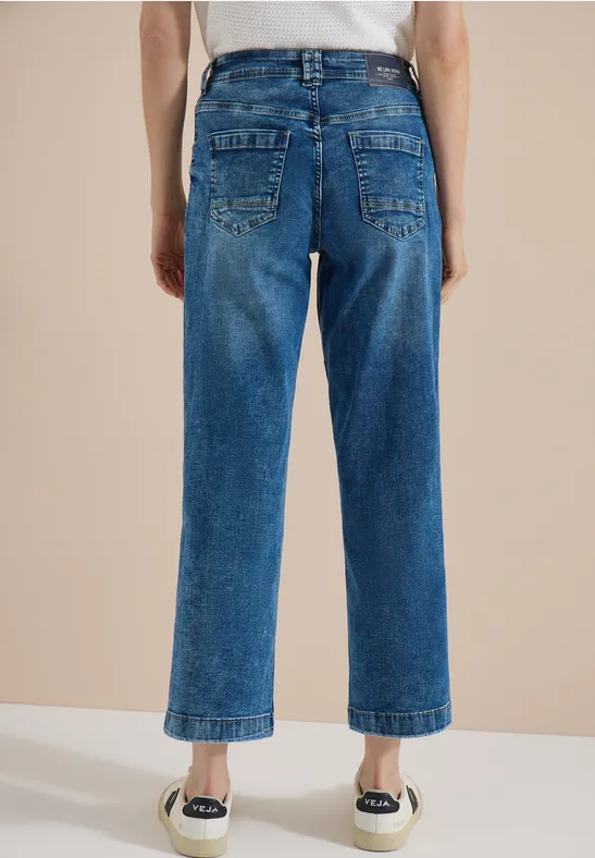 Vue arrière d’une personne portant un jean bleu droit, court et des espadrilles blanches.