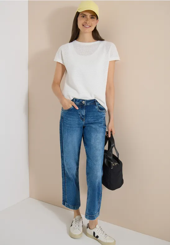 Femme en t-shirt blanc ample, jean taille haute droit, baskets blanches et sac en toile noir.