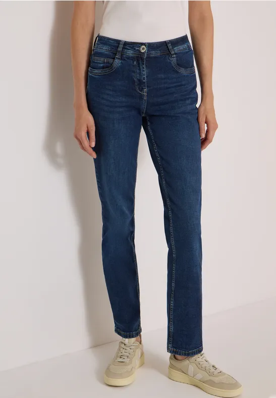 Eine Person trägt dunkelblaue Slim-Straight-Jeans mit hellen Sneakern.