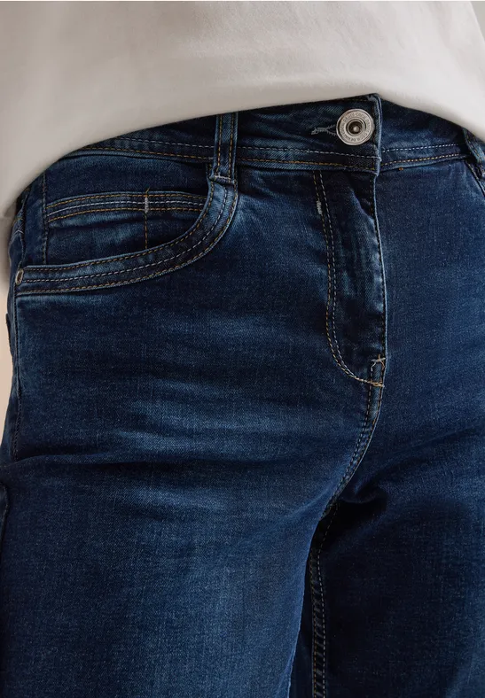 Nahaufnahme einer Person in dunkler Jeans mit Knopf und Teil eines weißen Oberteils