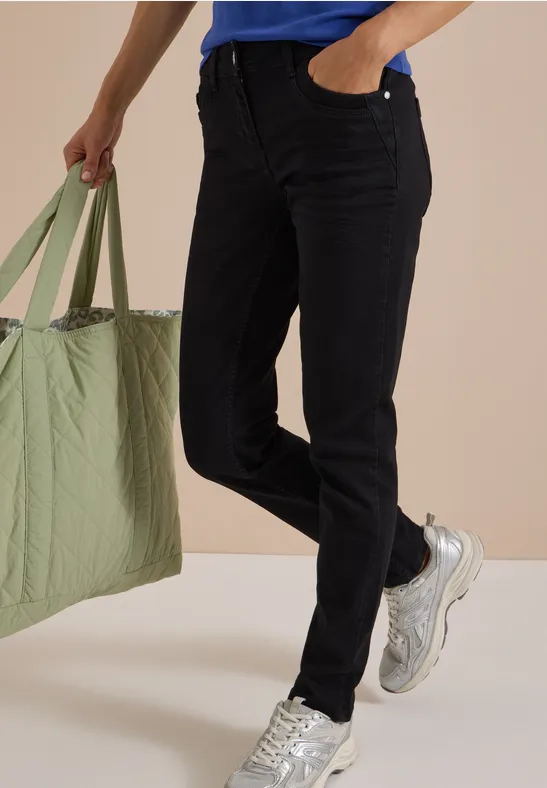 Schwarze Jeans, blaues Shirt, grüne gesteppte Tasche und weiße Sneaker an einer laufenden Person.
