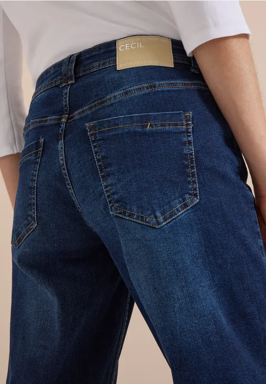 Rückansicht einer Person in blauen Jeans mit dezentem Label und weißem Oberteil.