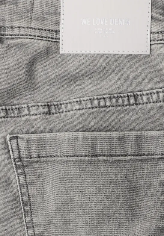 Close-up van de achterkant van een grijze spijkerbroek met achterzak, lussen en label “WE LOVE DENIM”.