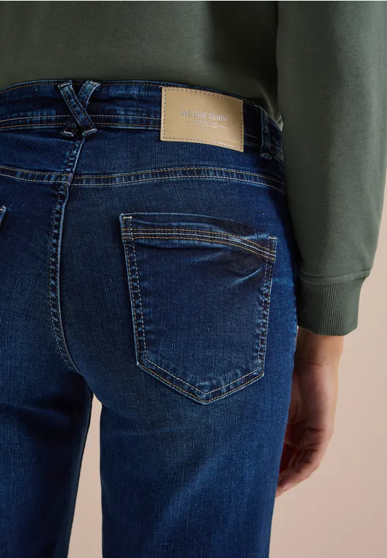 Eine Person trägt dunkle Jeans und ein grünes Sweatshirt, Ansicht von hinten.