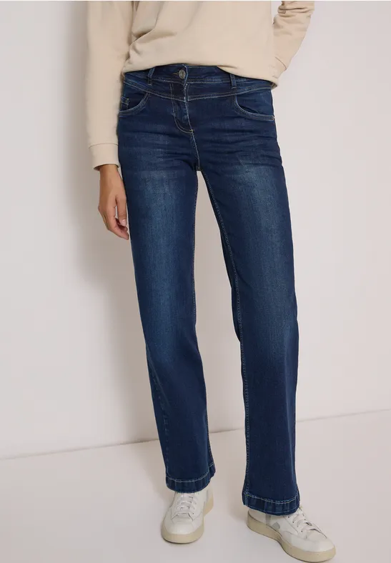 Eine Person trägt dunkelblaue, gerade geschnittene Jeans und weiße Sneaker.