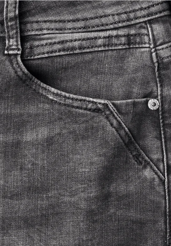 Close-up van een donkerblauwe spijkerbroek met achterzak, stiksels en een klinknagel.