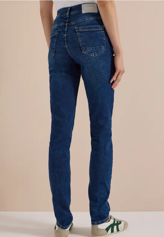 Nahaufnahme von einer Person von hinten in dunkelblauen Jeans und weißen Sneakers mit grünen Streifen.