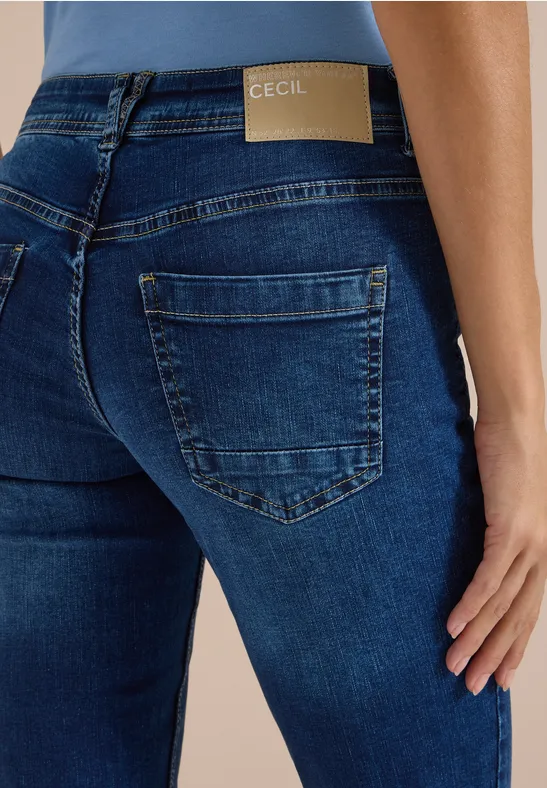 Vue arrière d'une femme en jean bleu moulant avec étiquette 'CECIL' à la taille.