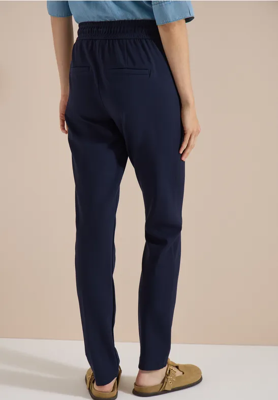Personne de dos en pantalon droit bleu marine à taille élastique et mocassins beiges sur fond clair.
