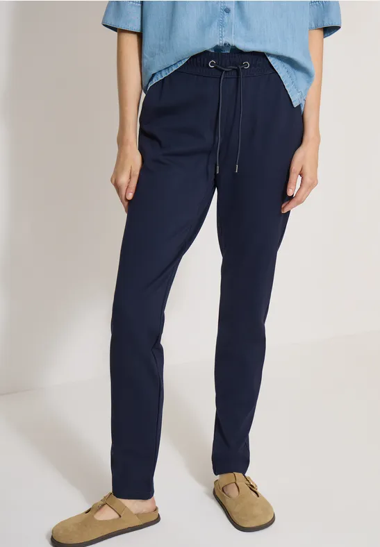 Une personne porte un pantalon bleu marine décontracté avec cordon et des mules beiges.
