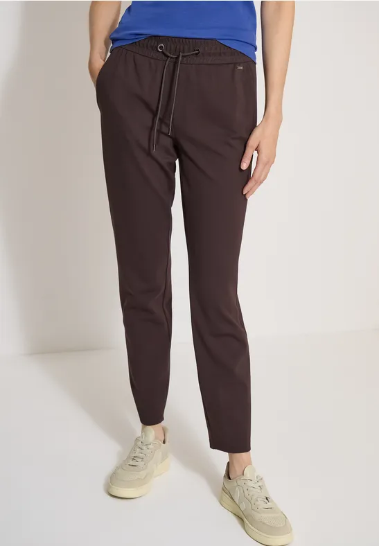 Donkerbruine, slanke broek met trekkoord in de taille, gecombineerd met beige sneakers.