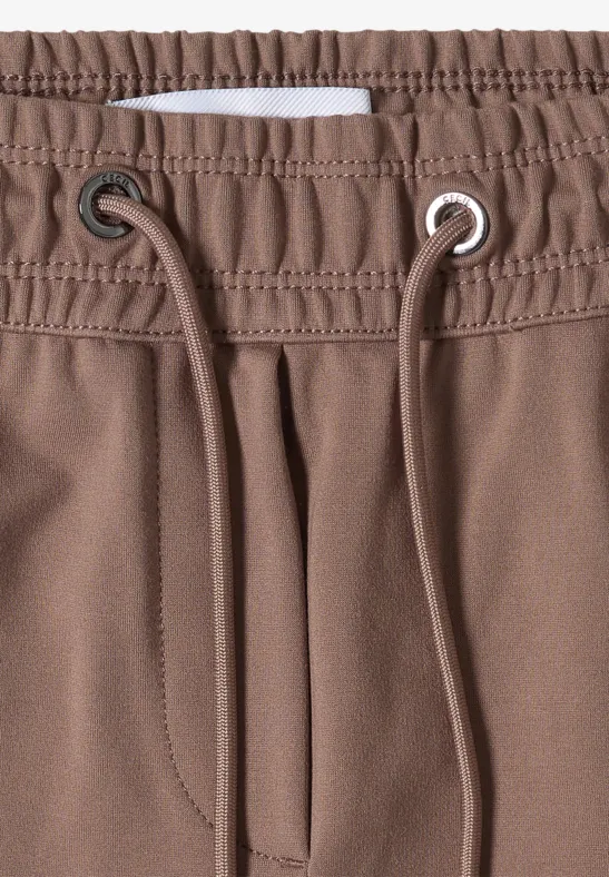 Nahaufnahme einer braunen Hose mit elastischem Bund und Kordelzug, sichtbaren Ösen und Nahtdetails.