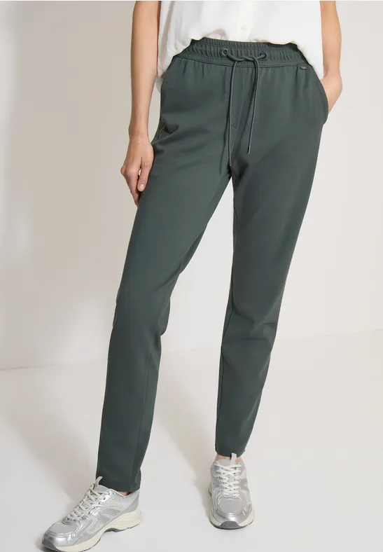 Model draagt een donkergroene casual broek met trekkoord en zilverkleurige sneakers.