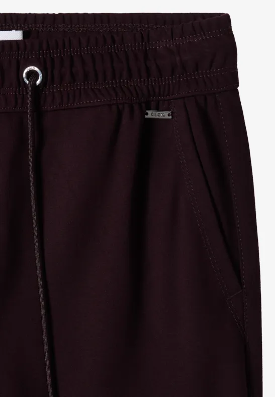 Gros plan sur un pantalon de jogging bordeaux avec ceinture élastique, cordon de serrage et poche latérale.