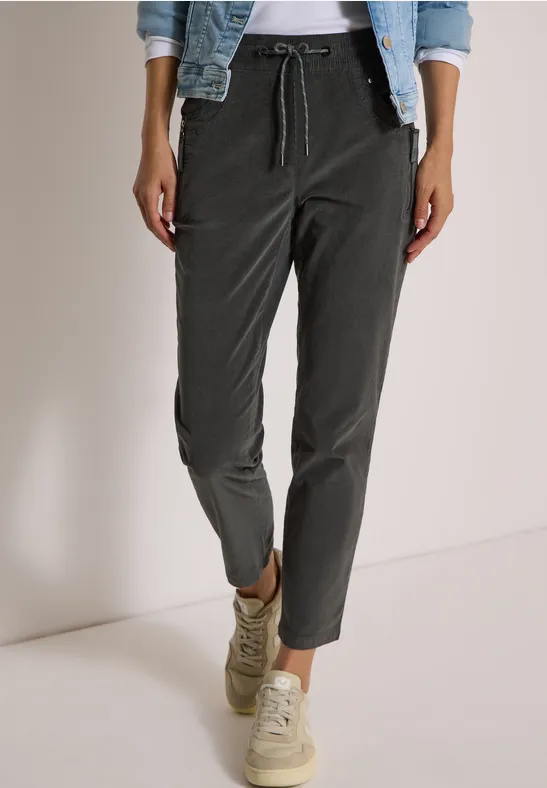 Dunkelgraue, lässige Hose mit Tunnelzug, kombiniert mit hellen Sneakers und Jeansjacke.