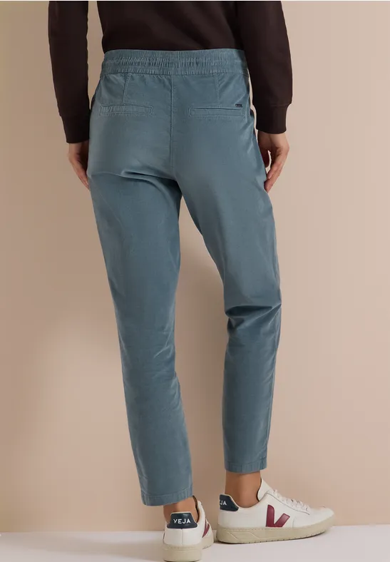 Taillierte, türkise Hose mit elastischem Bund und Taschen, kombiniert mit weißen Sneakern vor beigem Hintergrund.