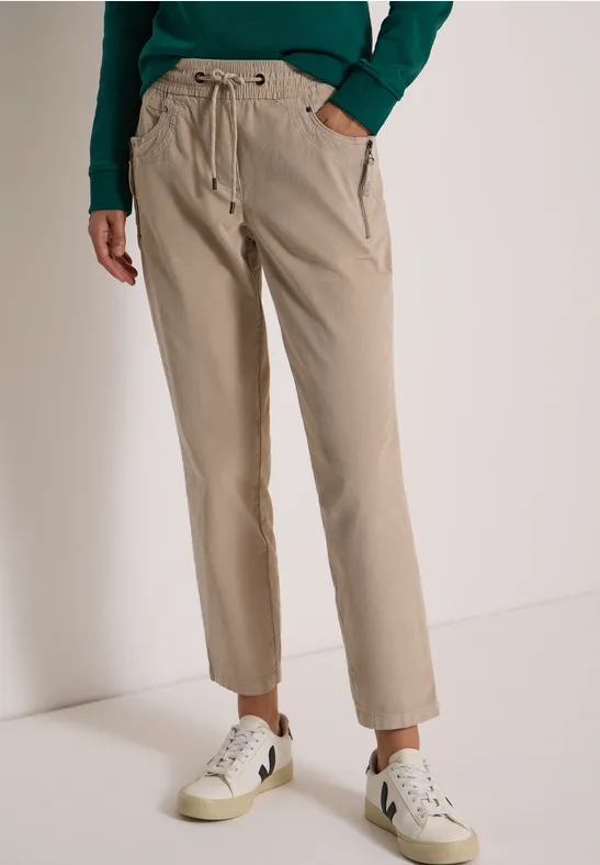 Model trägt beige Hose mit Kordelzugbund, seitlichen Taschen und weißen Sneakern, lässiger Look.