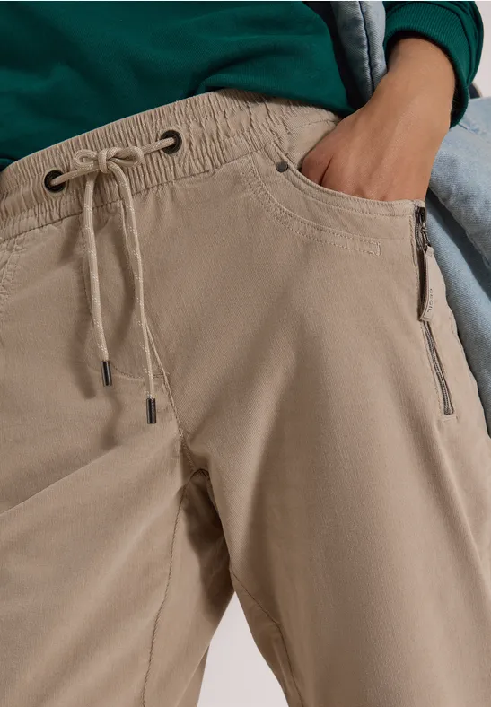 Nahaufnahme einer Person in beigen Hosen mit Tunnelzug und Taschen, Hand in der Tasche.