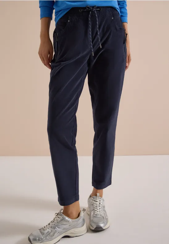 Eine Person trägt dunkelblaue Jogginghose mit Bündchen und silbergraue Sneakers vor hellem Hintergrund.