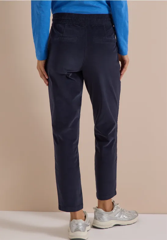 Eine Person steht von hinten, trägt eine marineblaue Cordhose, blauen Pullover und weiße Sneaker.
