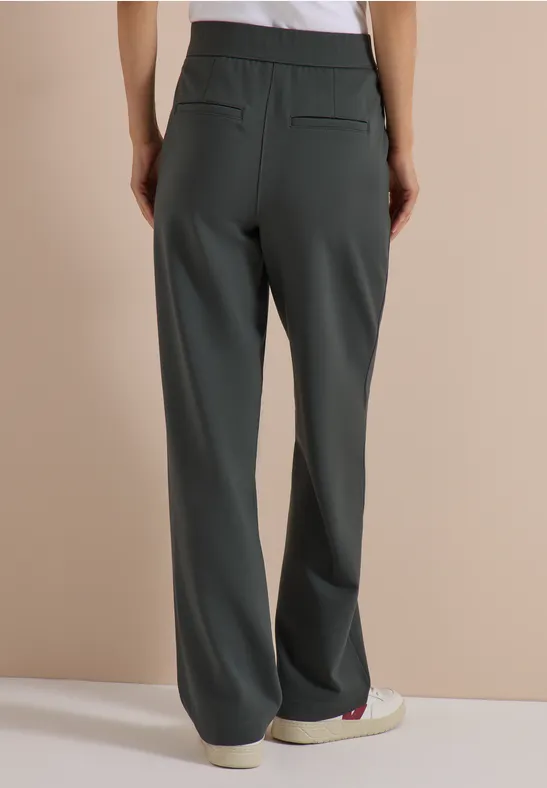 Femme portant un pantalon droit et ample gris foncé, vue de dos dans un style minimaliste.