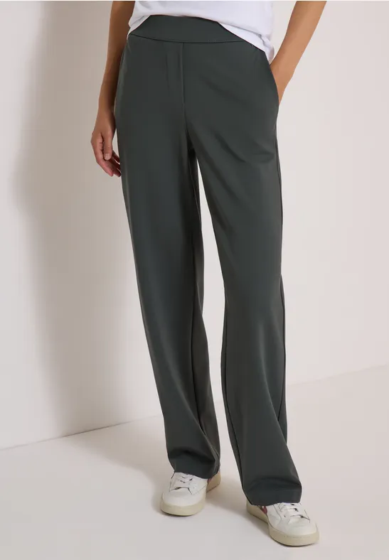 Pantalon femme ample vert foncé à coupe droite, poches latérales, porté avec des baskets blanches.