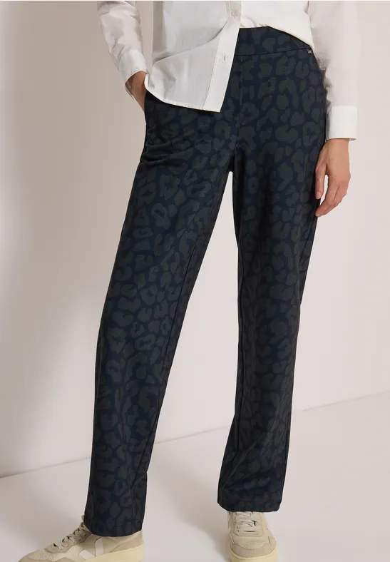 Dunkelblaue, gerade geschnittene Hose mit dezentem Muster, kombiniert mit weißer Bluse und hellen Sneakern.