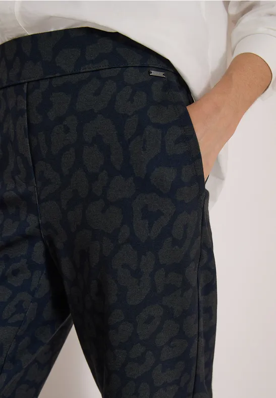 Nahaufnahme einer dunklen, leopardenmusternden Hose mit seitlicher Tasche und weißem Oberteil