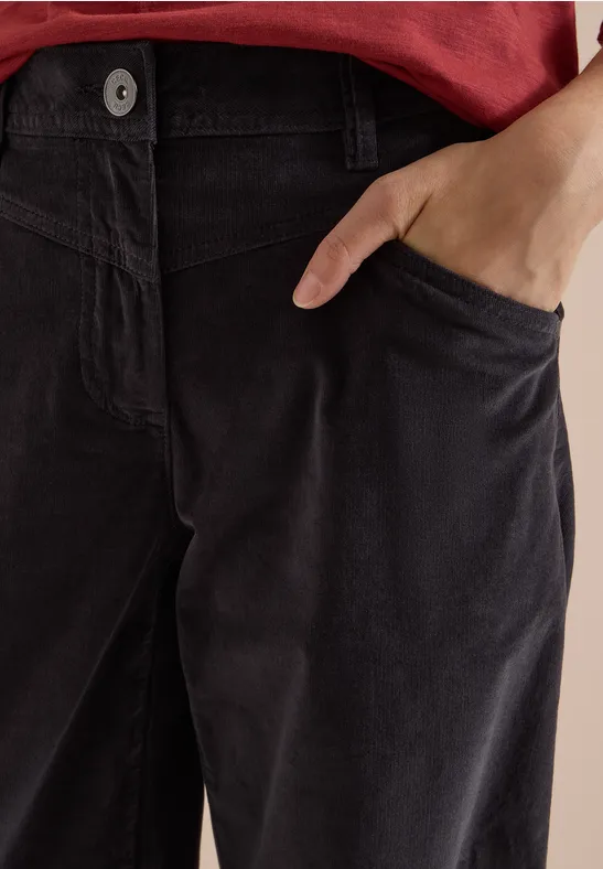 Gros plan d'une personne en haut rouge et pantalon en velours côtelé sombre, main dans la poche.