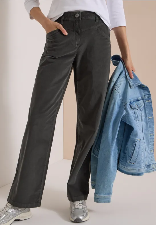 Personne porte un pantalon noir large avec poches, un haut blanc, baskets argentées et tient une veste en jean claire.