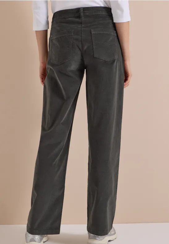 Vue de dos d'une personne portant un pantalon large en velours côtelé gris et des baskets blanches.