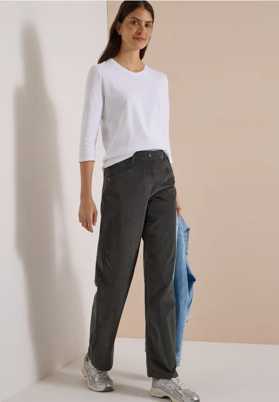 Femme en t-shirt blanc 3/4, jeans noirs et baskets, tenant une veste bleu clair décontractée à la main.
