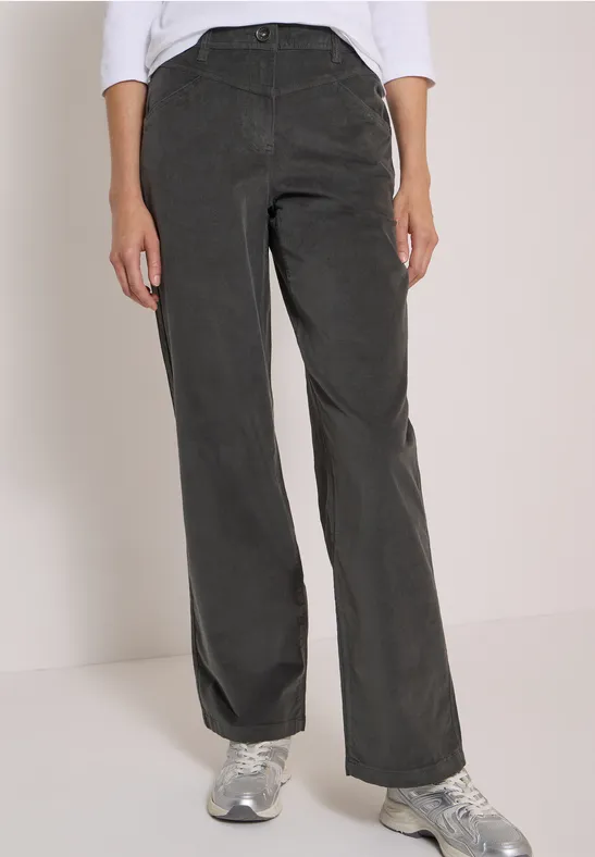 Femme en pantalon en velours côtelé gris foncé à jambes larges et baskets, sur fond clair.