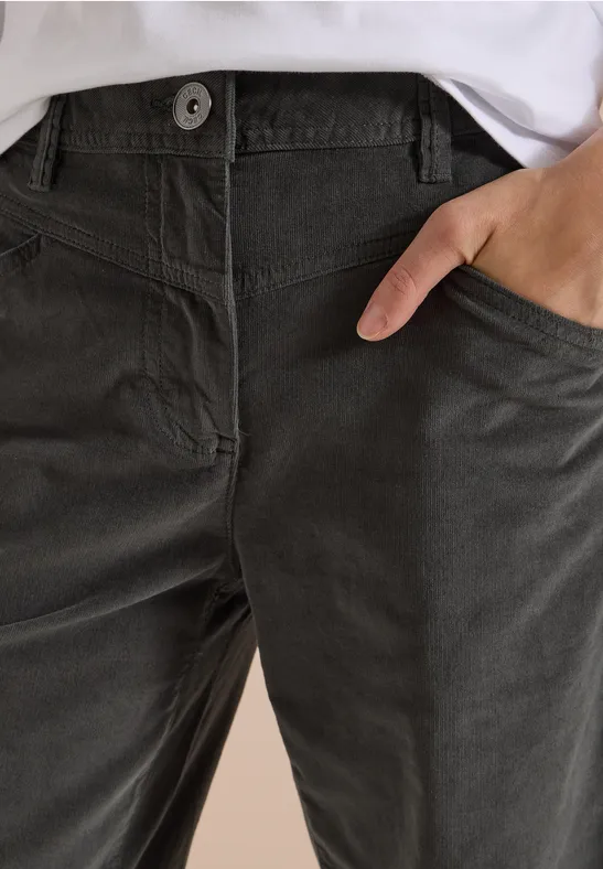 Pantalon en velours côtelé gris foncé, main posée dans la poche latérale