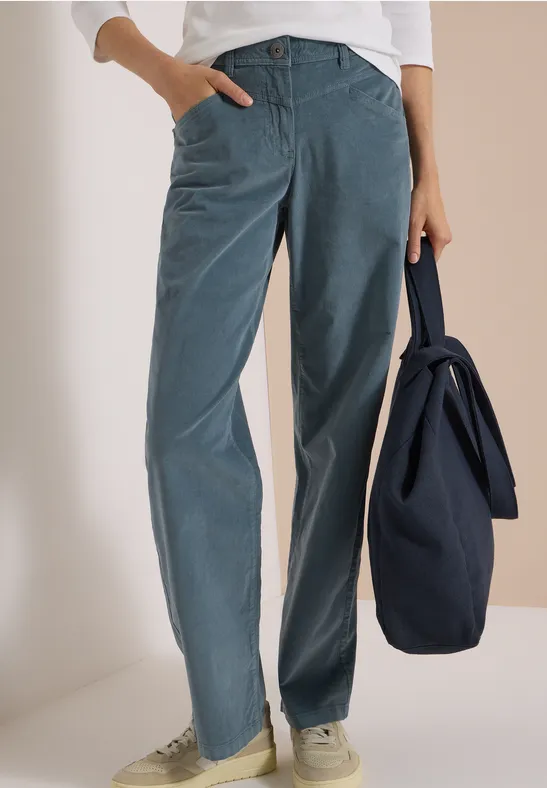 Femme portant un pantalon large en velours côtelé bleu, baskets blanches, haut blanc, tenant un sac bleu marine.