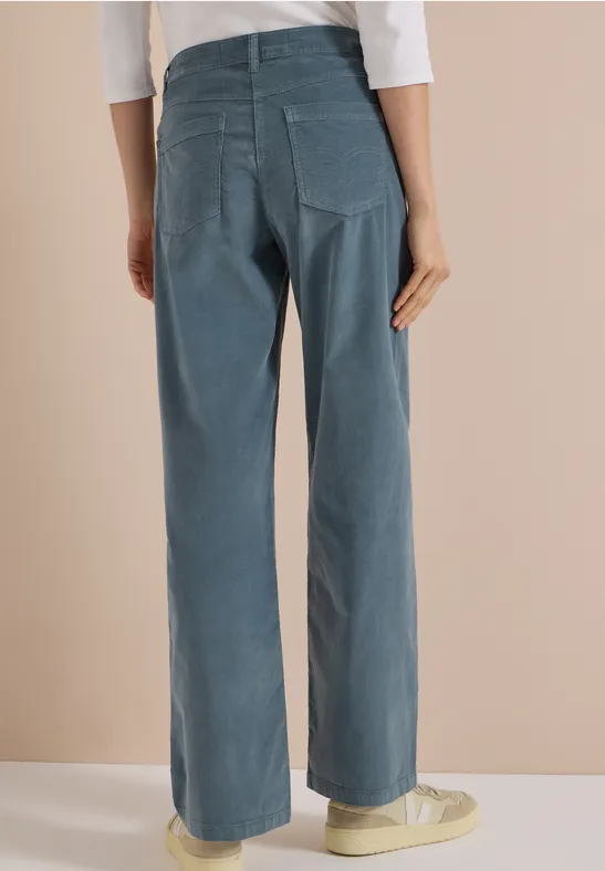 Vue arrière d'une personne portant un pantalon large en velours côtelé bleu et des baskets claires.