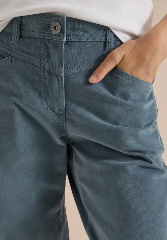 Gros plan sur un pantalon bleu en coton, main dans la poche et bord supérieur blanc visible.