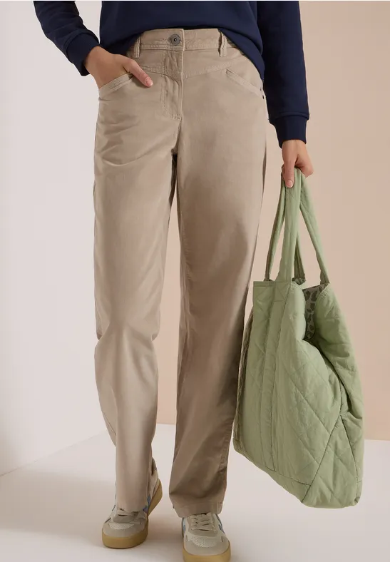 Vue de la partie basse du corps, pantalon beige ample, baskets vert pâle et sac matelassé vert.