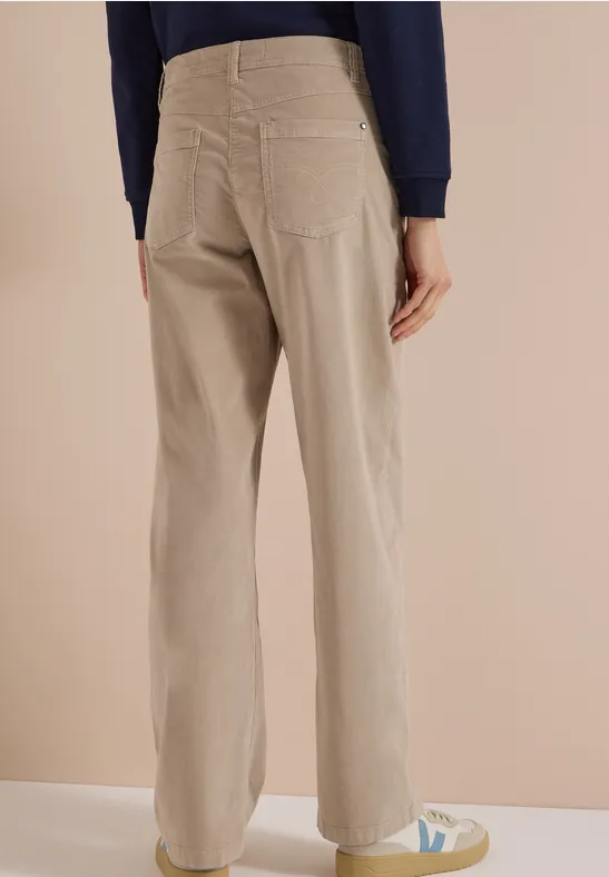 Personne vue de dos en pantalon beige à jambes larges et baskets blanches sur fond neutre.