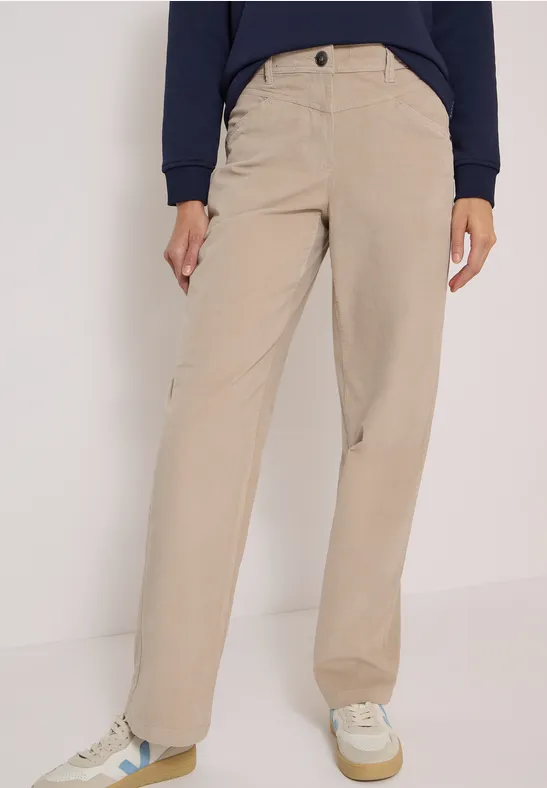 Personne portant un pantalon en velours beige à jambes larges et des baskets blanches.