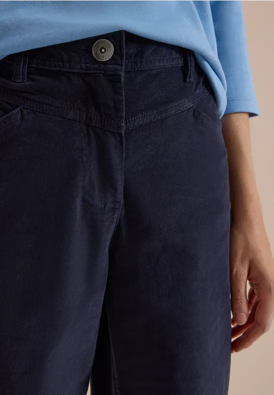 Vue rapprochée d'une personne portant un pantalon velours côtelé bleu foncé et un haut bleu clair, main sur le côté
