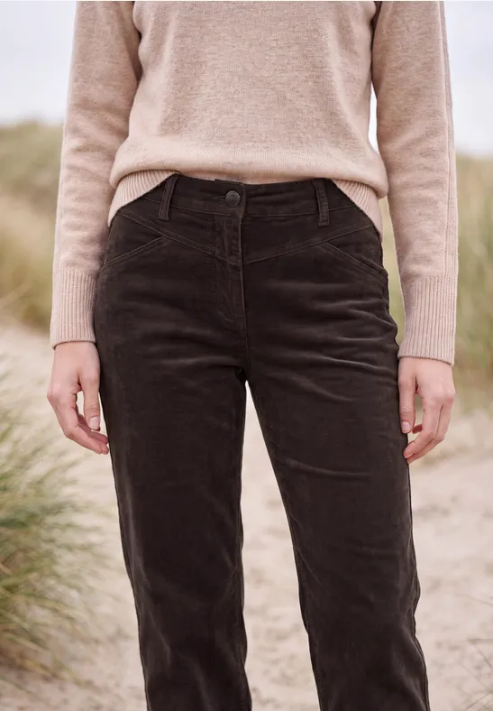 Person steht vor Dünengras am Strand, trägt einen beigen Pullover und schwarze Cordhose