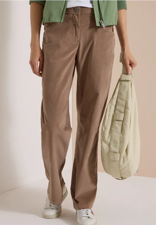 Personne porte un pantalon en velours marron, baskets blanches et tient un sac matelassé beige.