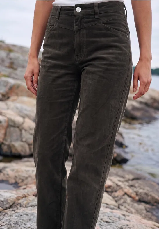 Eine Person steht auf Felsen und trägt eine dunkelbraune Cordhose.