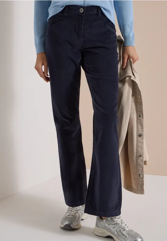 Personne porte un pantalon bleu foncé évasé, un pull bleu clair, des sneakers grises et tient un manteau beige.