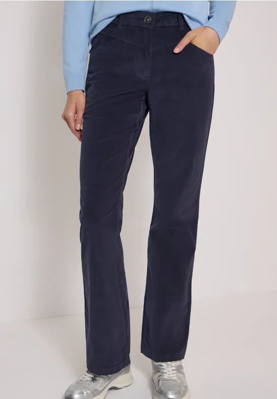 Pantalon en velours côtelé bleu foncé, coupe droite avec poches, porté avec baskets argentées et pull clair.